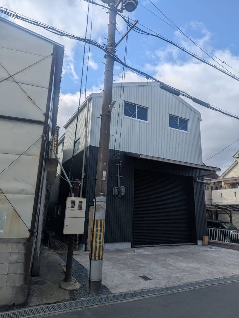 送電線と電柱が見える街区に建つ、ツートーン金属外壁の工場・倉庫